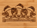 Close-up of Christmas cows engraved on warm honey-toned bamboo with natural grain visible.