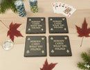 Four black slate coasters with humorous text on a wooden surface.