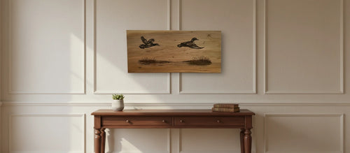 A rectangular wooden wall art piece featuring two flying ducks, displayed on a beige paneled wall above a dark wood console table with a small plant and books.