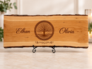 Personalized live-edge wedding board with Tree of Life engraving and custom names, shown on a display stand.